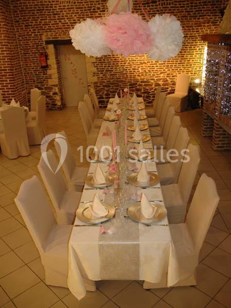 Table de banquet décorée avec nappes blanches, serviettes pliées, bougies roses et guirlandes, dans une salle en briques.