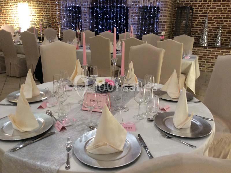Table élégamment dressée avec nappes blanches, serviettes pliées, chandeliers roses et décorations florales.