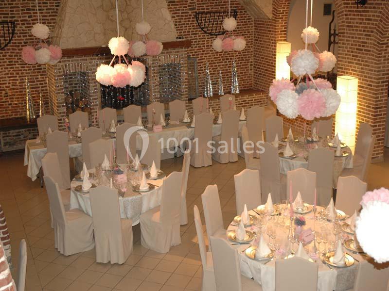 Salle de réception décorée avec des tables rondes dressées, des chaises couvertes et des suspensions en pompons roses et…