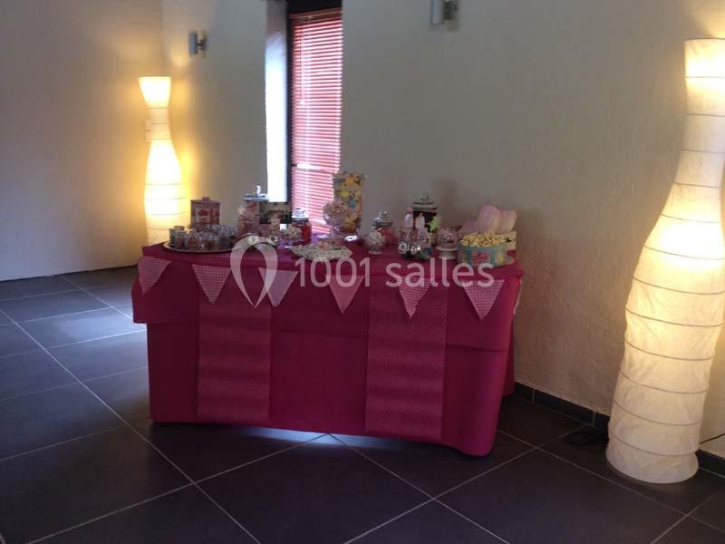 Table décorée avec une nappe rose, ornée de guirlandes et de friandises, entourée de lampes dans une pièce lumineuse.