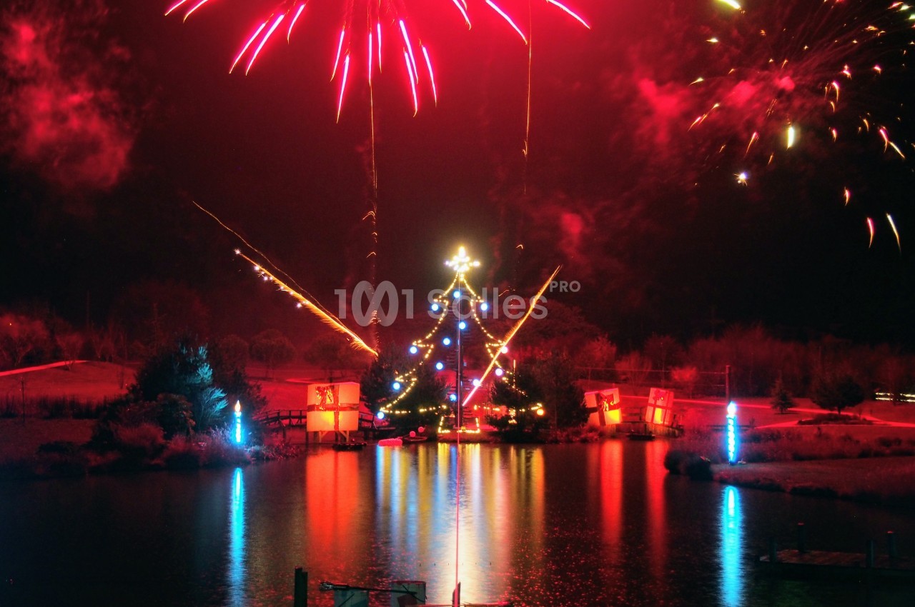 Feu d'artifice illuminant un lac avec des décorations lumineuses et des reflets colorés sur l'eau.