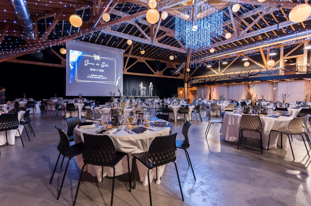 Salle de réception décorée avec des tables dressées, des guirlandes lumineuses et un écran de projection.