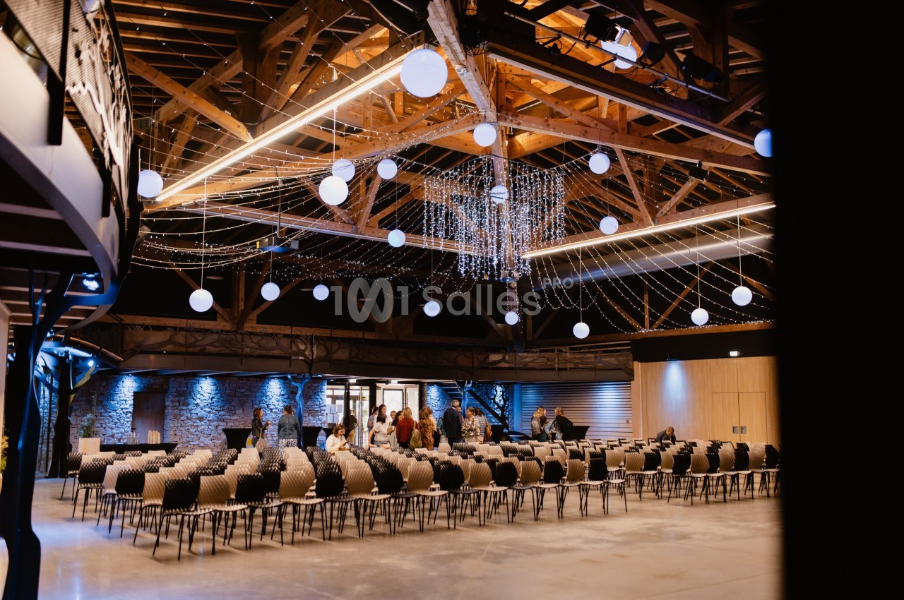 Salle spacieuse avec des chaises alignées, éclairage chaleureux et décorations lumineuses suspendues au plafond en bois.