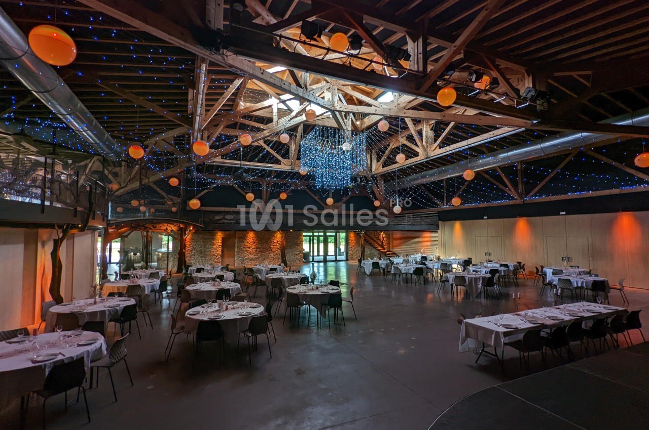 Salle de réception spacieuse avec des tables dressées, éclairage tamisé et décoration lumineuse suspendue.