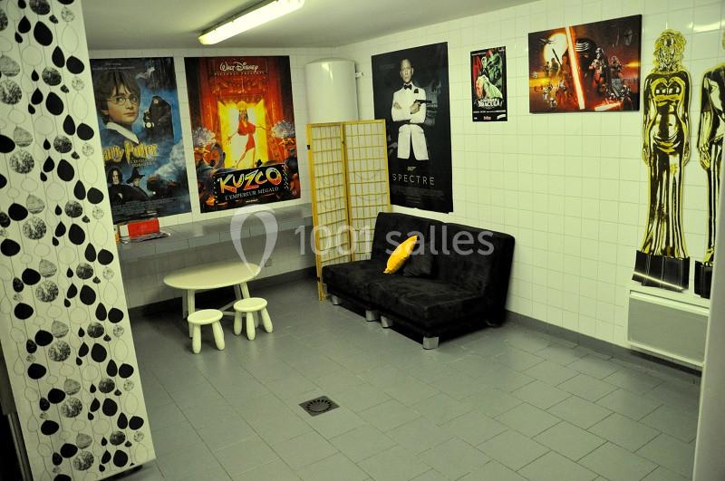 Salle carrelée avec canapé noir, table basse et affiches de films sur les murs.