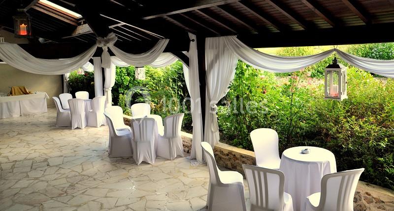 Terrasse couverte décorée de voilages blancs, avec tables et chaises blanches, donnant sur un jardin verdoyant.