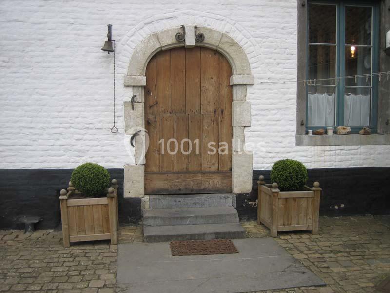 Porte en bois ancienne avec encadrement en pierre, flanquée de deux bacs à plantes sur un sol pavé.
