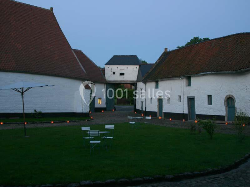 Cour intérieure pavée entourée de bâtiments anciens aux murs blancs et toits en tuiles, éclairée par des bougies au sol.