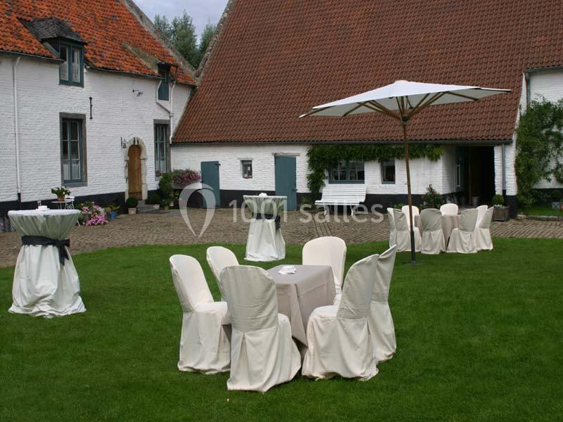 Chaises et tables habillées de housses blanches disposées sur une pelouse devant des bâtiments à toits en tuiles.