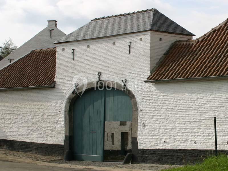 Porte cochère en bois bleu encadrée par des murs en briques blanches et un toit en tuiles rouges.