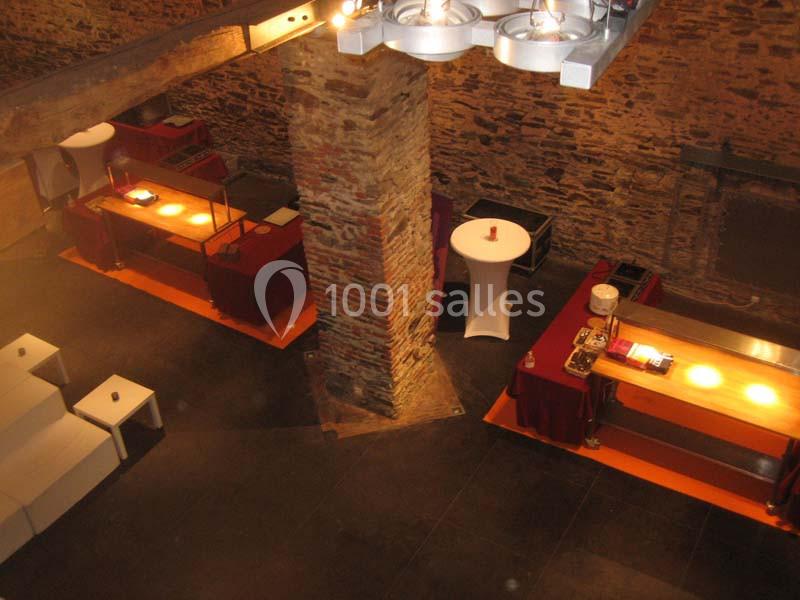 Salle en pierre avec poutres apparentes, tables éclairées pour buffet et mobilier de réception.