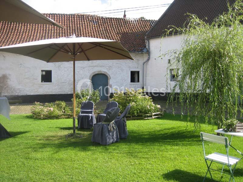 Cour verdoyante avec chaises et parasols, entourée de bâtiments blancs à toit en tuiles rouges.