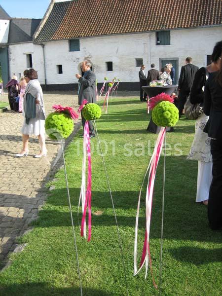 Décoration de jardin avec boules de fleurs vertes et rubans roses, lors d'un événement en extérieur.