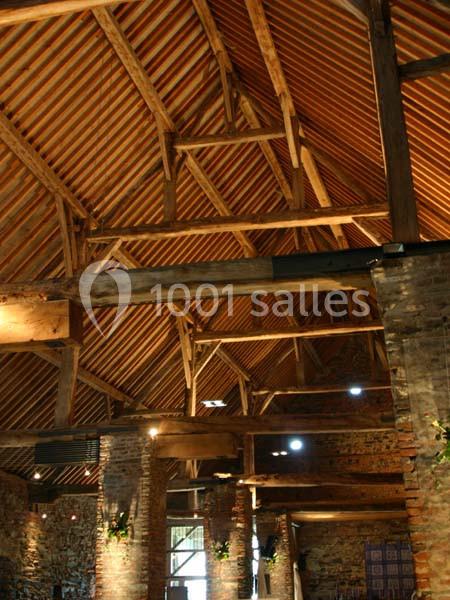 Charpente en bois apparente d'un bâtiment ancien avec des murs en briques et un éclairage intérieur chaleureux.