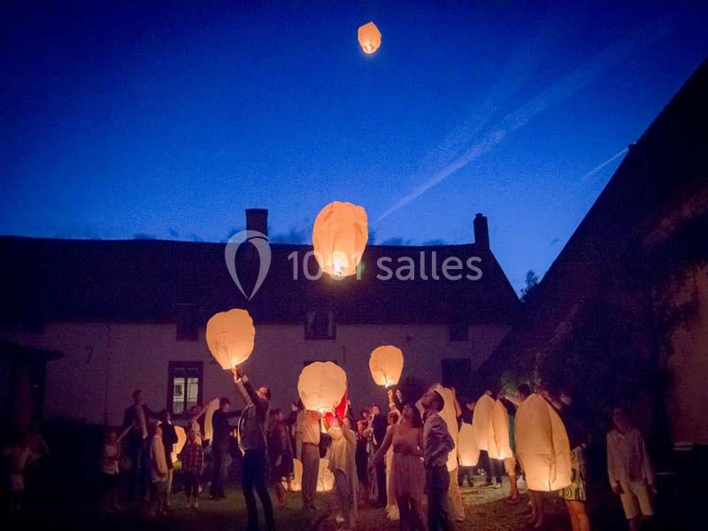 Des personnes rassemblées la nuit lancent des lanternes volantes illuminées dans un ciel sombre.