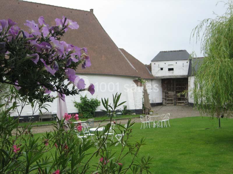 Cour verdoyante avec mobilier de jardin blanc, fleurs au premier plan et bâtiments en briques blanches en arrière-plan.