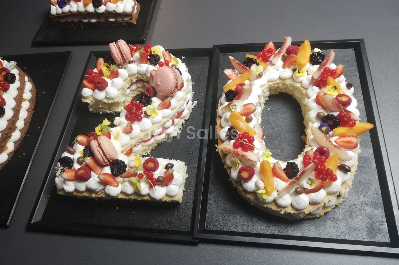 Gâteau en forme du chiffre 20, décoré de fruits frais, macarons et crème, présenté sur un plateau noir.