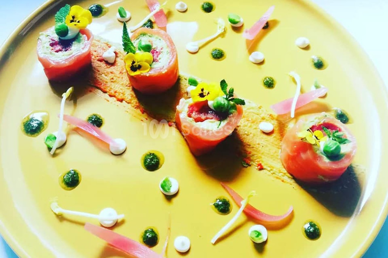 Assiette gastronomique avec roulés de saumon, purée, herbes, fleurs comestibles et décorations colorées.