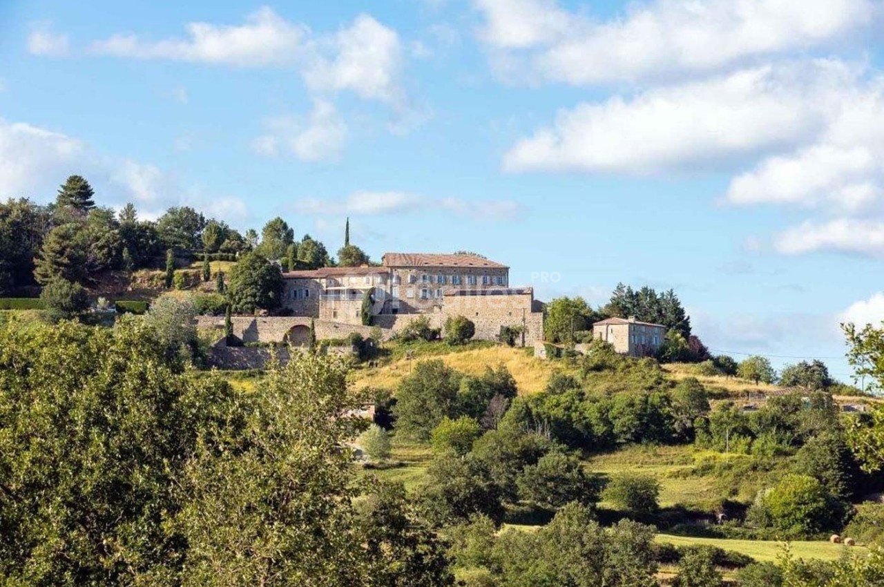 Vue d'un village perché avec des bâtiments en pierre entourés de végétation sous un ciel partiellement nuageux.