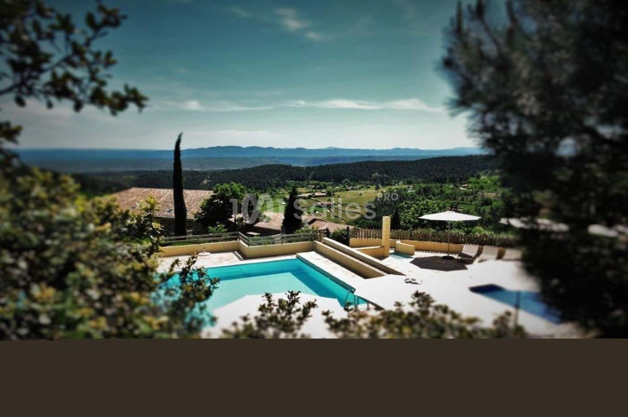 Vue d'une piscine entourée de végétation, avec un paysage vallonné et ensoleillé à l'arrière-plan.
