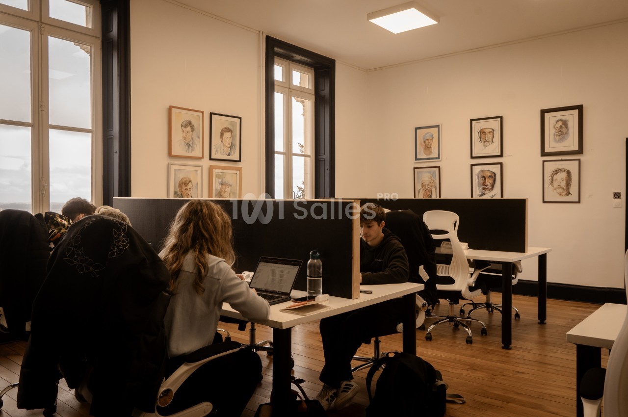 Personnes travaillant sur des ordinateurs dans un espace de coworking lumineux avec des portraits accrochés aux murs.