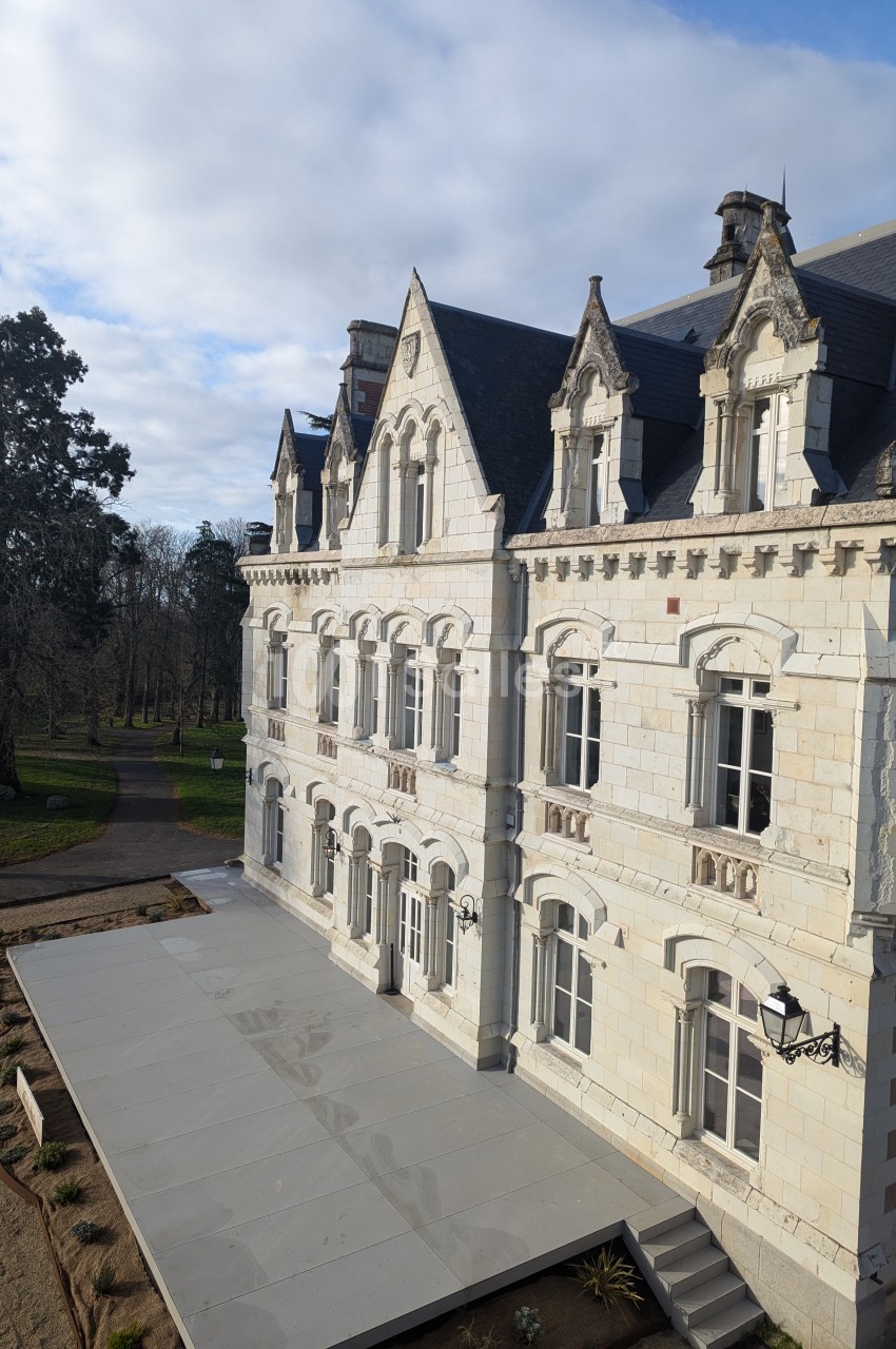 Façade d'un bâtiment historique en pierre blanche avec des toits en ardoise, entouré d'un parc arboré.