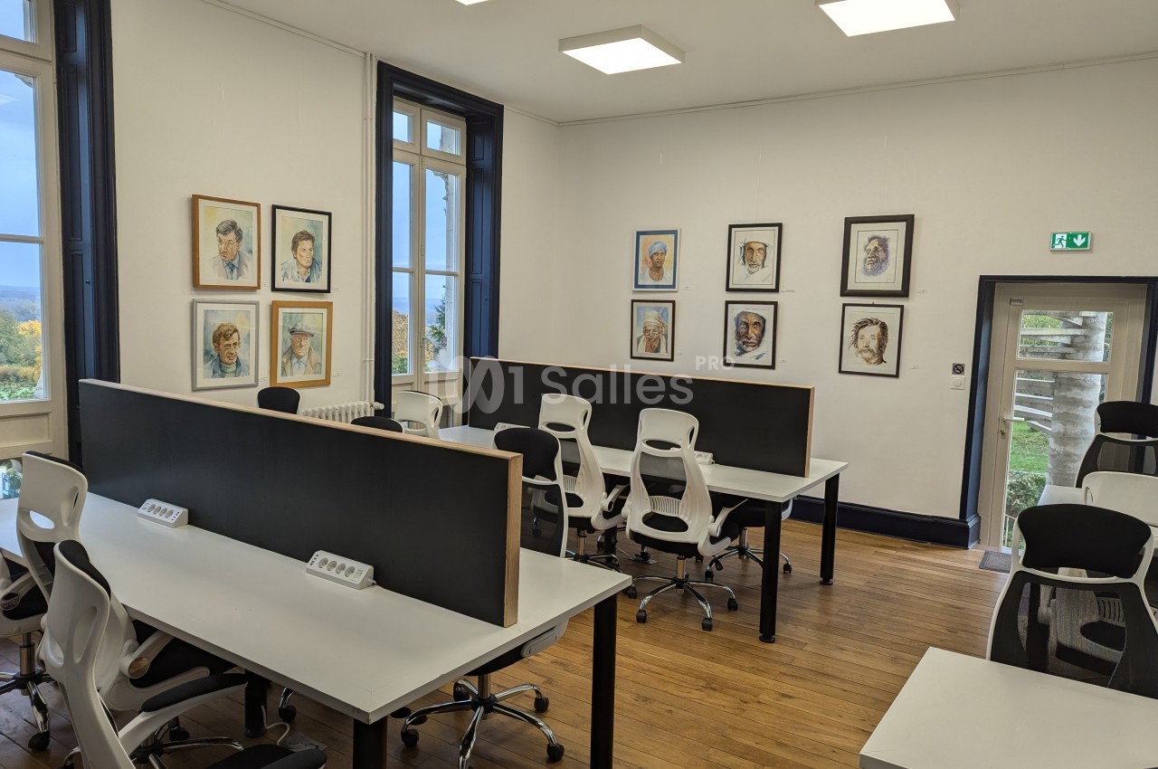 Salle de travail lumineuse avec des bureaux partagés, des chaises ergonomiques et des portraits accrochés aux murs.