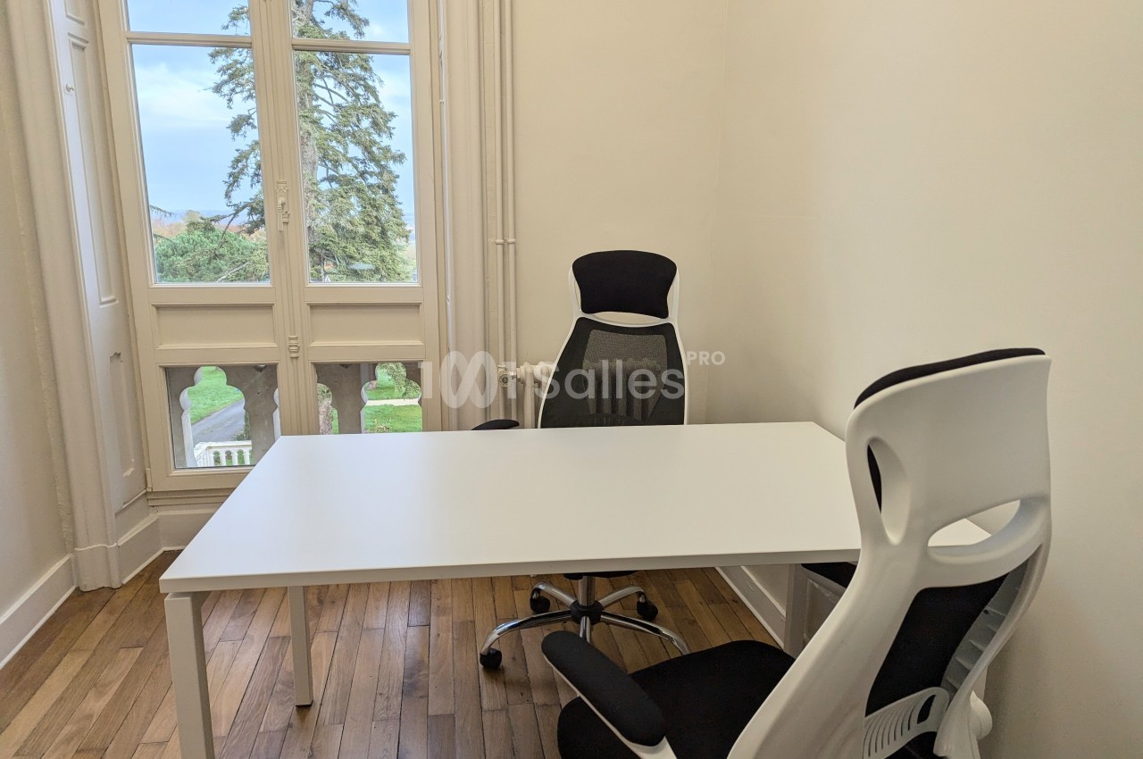 Deux chaises de bureau autour d'une table blanche dans une pièce lumineuse avec parquet et vue sur un jardin.