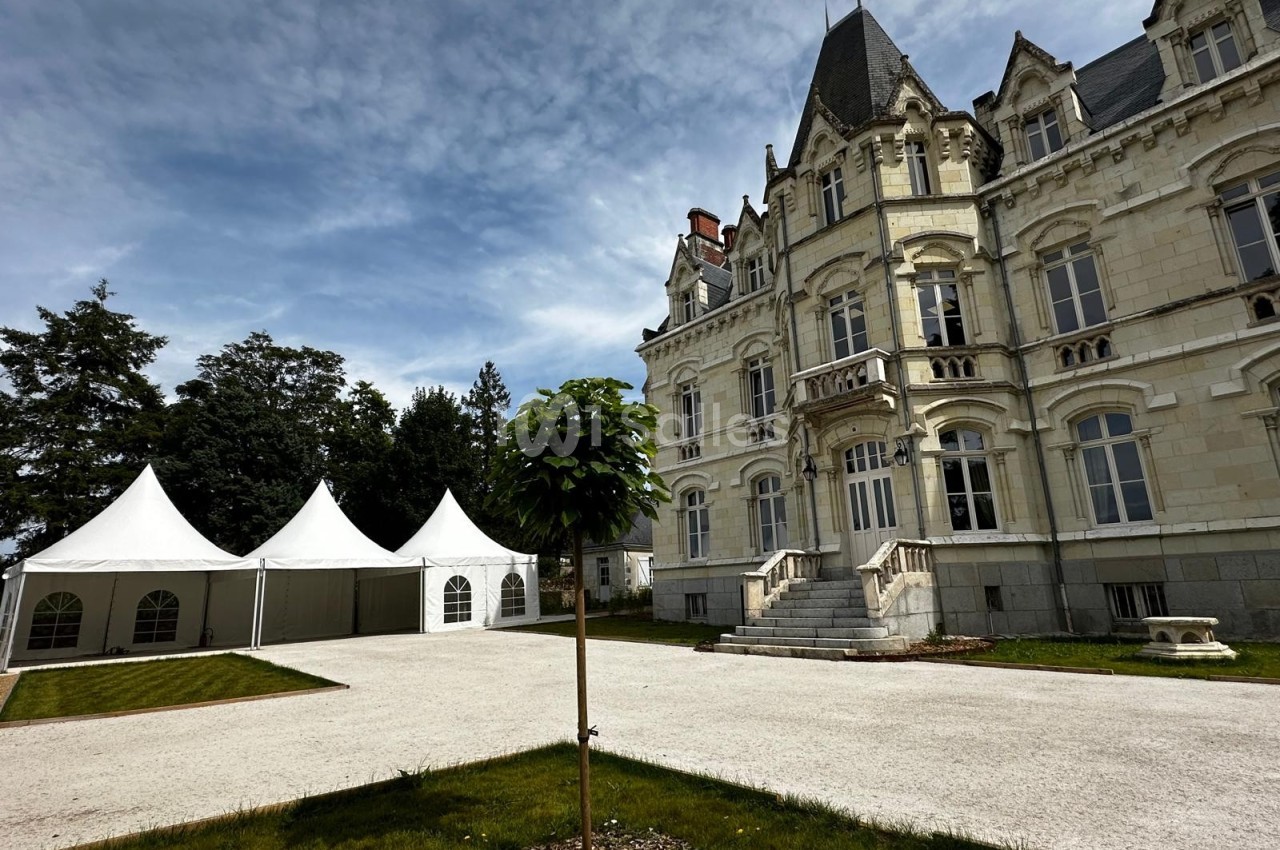 Façade d'un château en pierre avec des tentes blanches installées sur une pelouse et un arbre au premier plan.