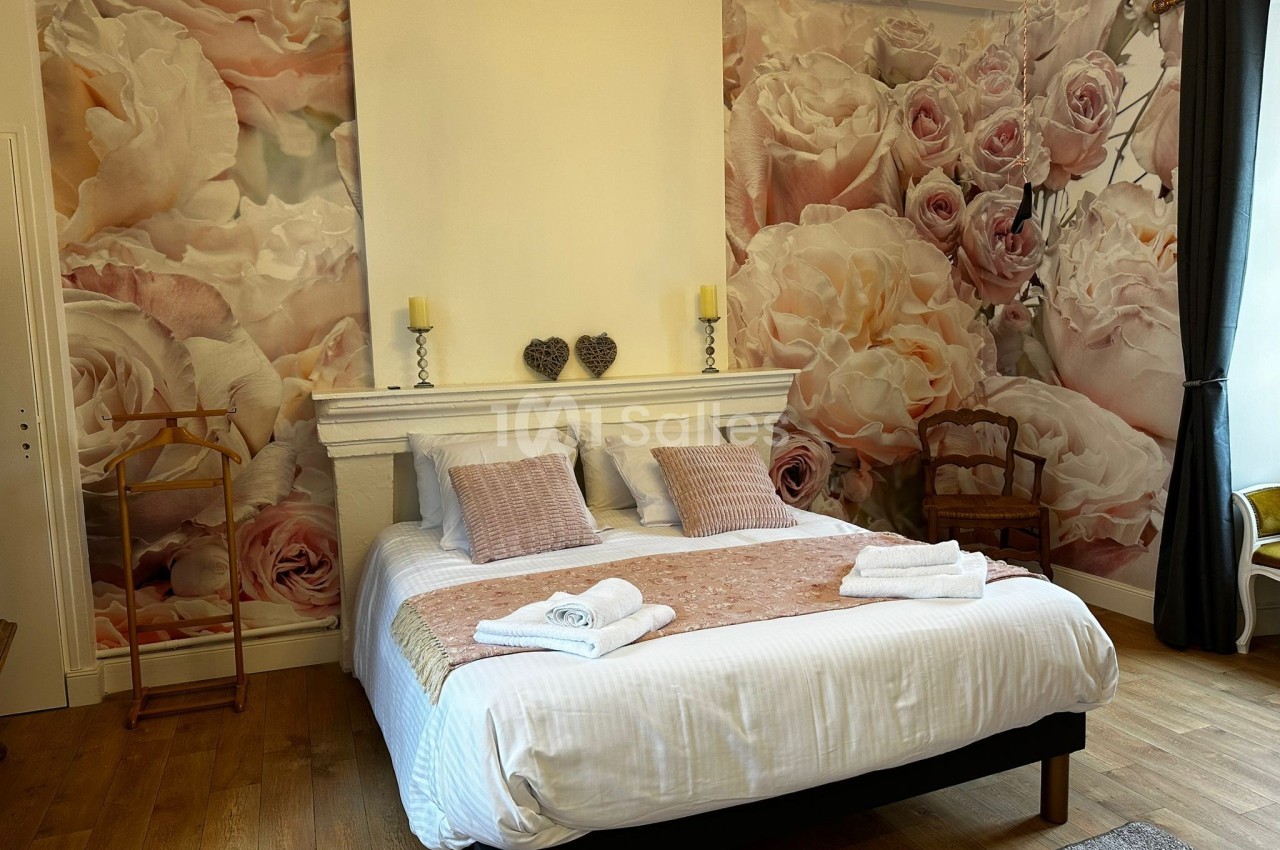 Chambre avec lit double, linge de lit clair, décor floral mural, parquet et mobilier en bois.