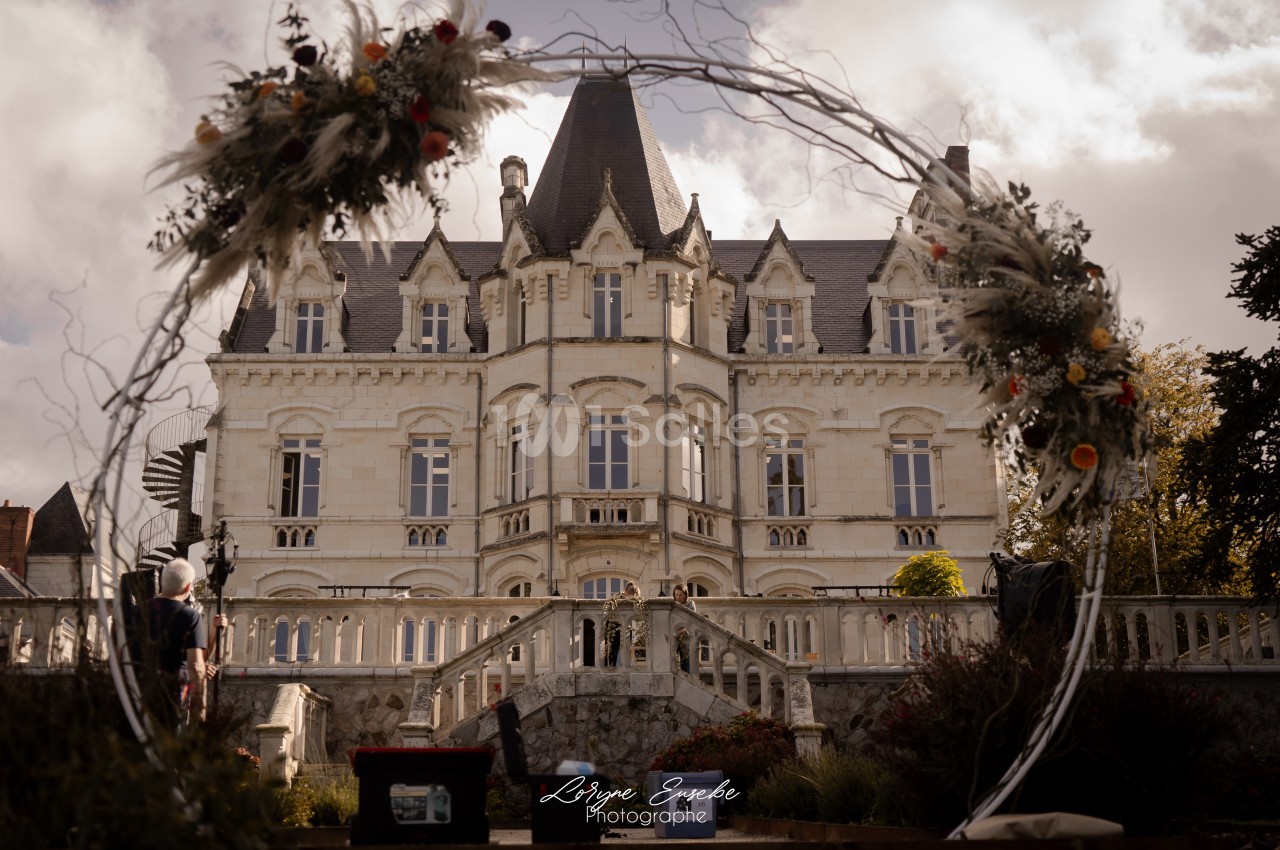 Façade d'un château en pierre blanche entouré de végétation, vue à travers un cercle décoratif fleuri.