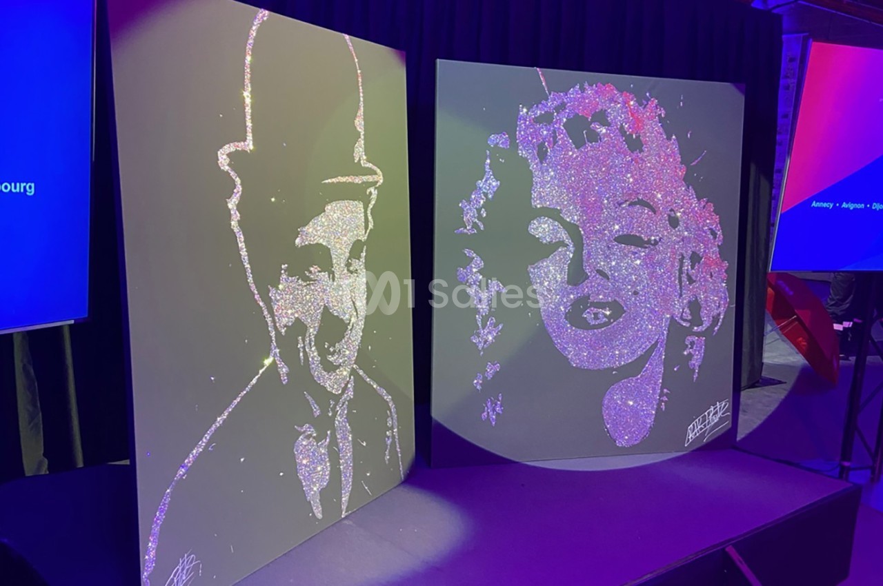 Deux tableaux scintillants représentant Charlie Chaplin et Marilyn Monroe sur une scène sombre.