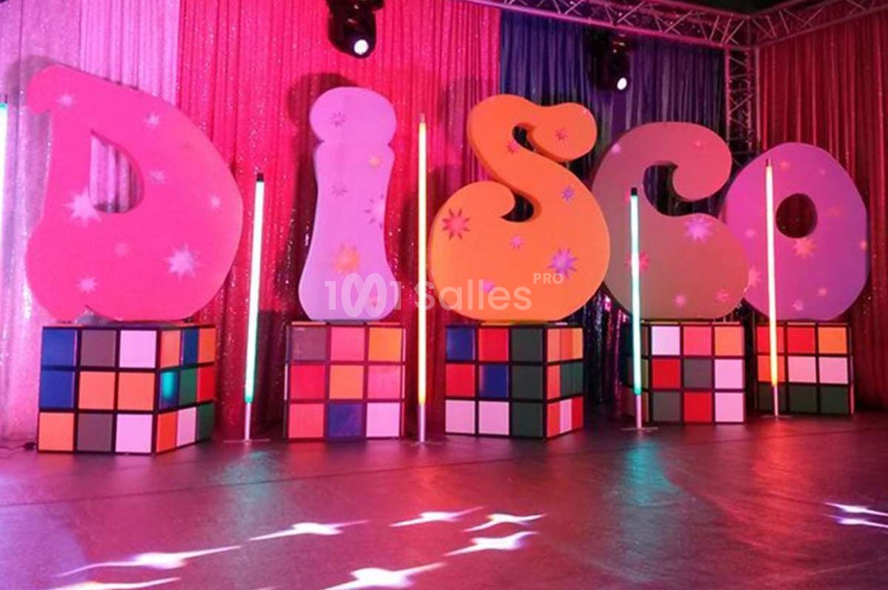 Décor coloré avec des lettres formant ’DISCO’ posées sur des cubes lumineux, entourées de rideaux scintillants.