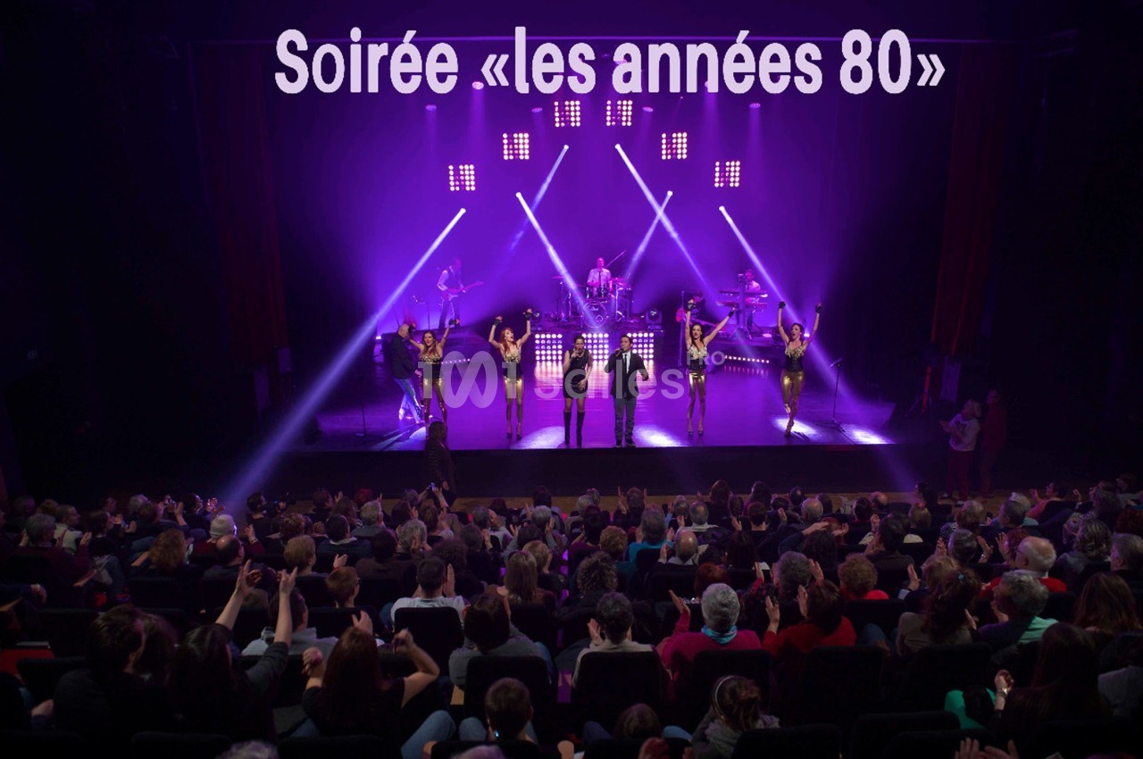 Spectacle sur scène avec musiciens et danseurs, éclairage violet, devant un public assis dans une salle comble.