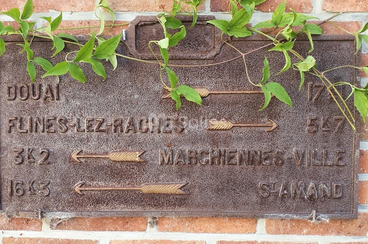 Plaque directionnelle en métal rouillé indiquant des distances vers plusieurs villes, accrochée sur un mur de briques avec…