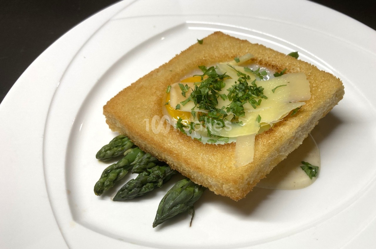 Toast doré avec œuf coulant, asperges vertes et copeaux de fromage, servi sur une sauce crémeuse.