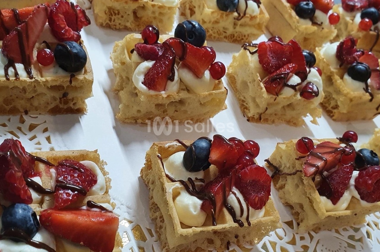 Gaufres garnies de crème, fruits rouges et myrtilles, décorées de filet de chocolat, présentées sur un plateau.