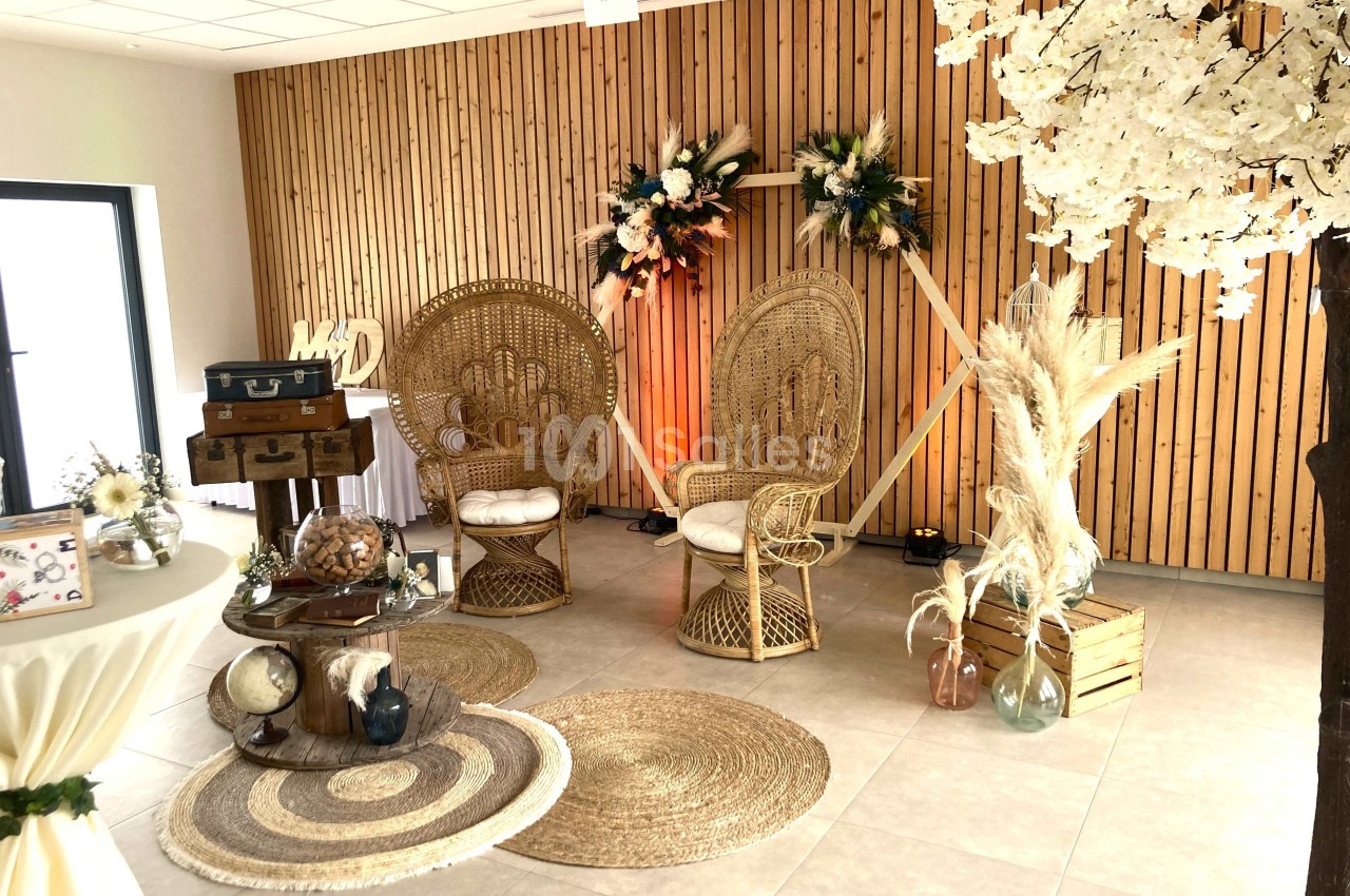 Décoration intérieure avec fauteuils en rotin, tapis en jute, fleurs séchées et éléments vintage dans une pièce boisée.
