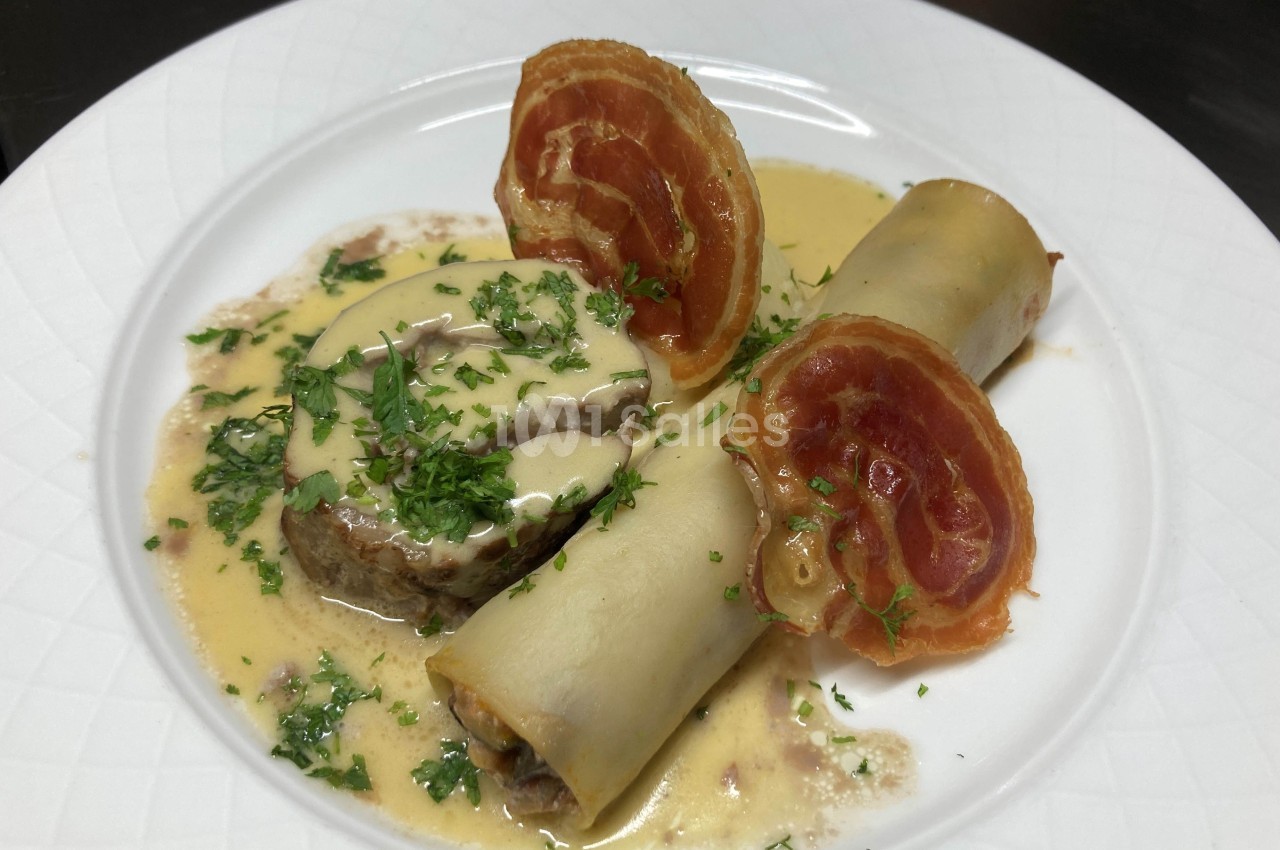 Assiette composée de cannellonis garnis, sauce crémeuse, tranche de viande et chips de jambon, décorée de persil.