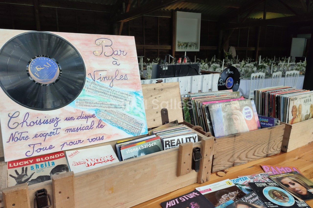 Disques vinyles exposés dans des caisses en bois, avec une pancarte indiquant ’Bar à Vinyles’ dans un cadre rustique.