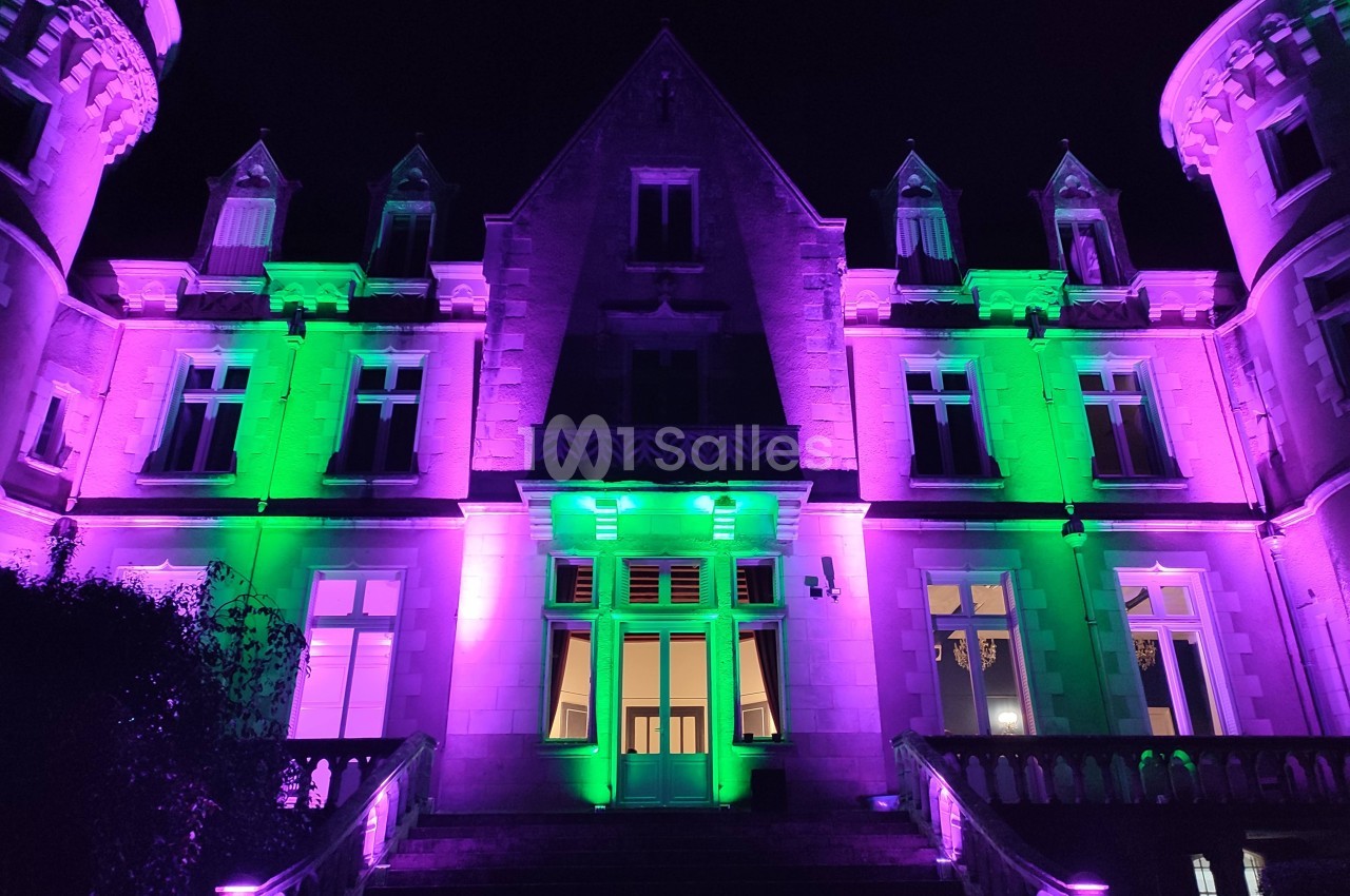 Façade d'un bâtiment ancien éclairé par des lumières violettes et vertes, vue de nuit.