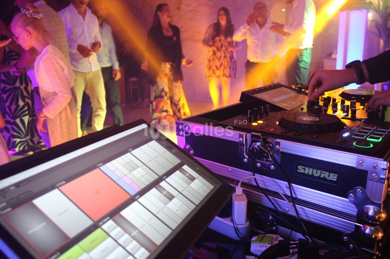Vue d'une table de mixage et d'un écran de contrôle lors d'une soirée dansante avec des invités en arrière-plan.