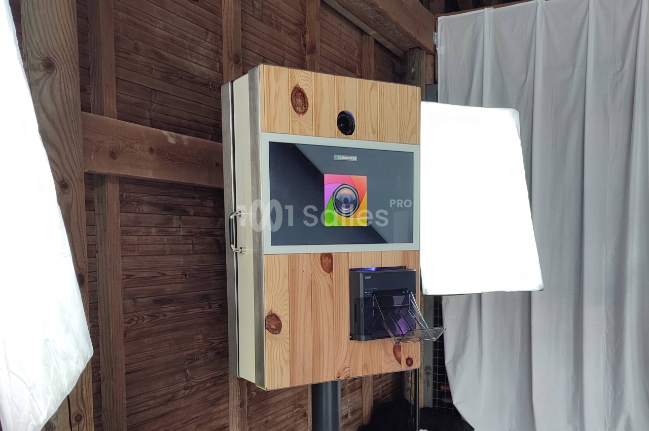 Borne photo en bois avec écran, appareil photo intégré et imprimante, installée dans un espace intérieur en bois.
