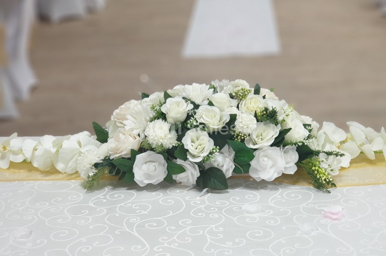 Arrangement floral blanc sur une table recouverte d'une nappe ornée de motifs, dans une salle de réception.