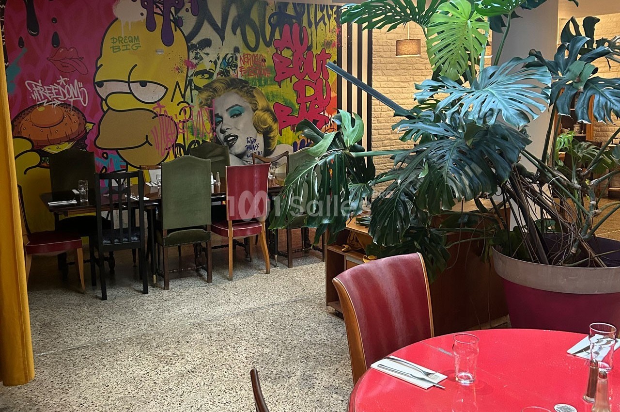 Salle de restaurant colorée avec des graffitis sur les murs, des plantes vertes et des tables dressées.