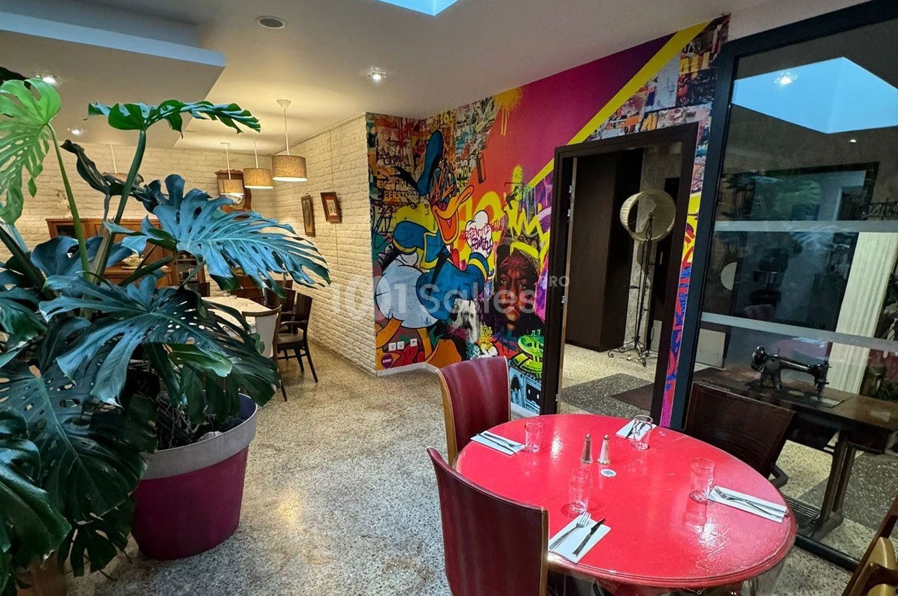 Salle de restaurant colorée avec mur décoré de fresques urbaines, plantes en pot et table rouge dressée.