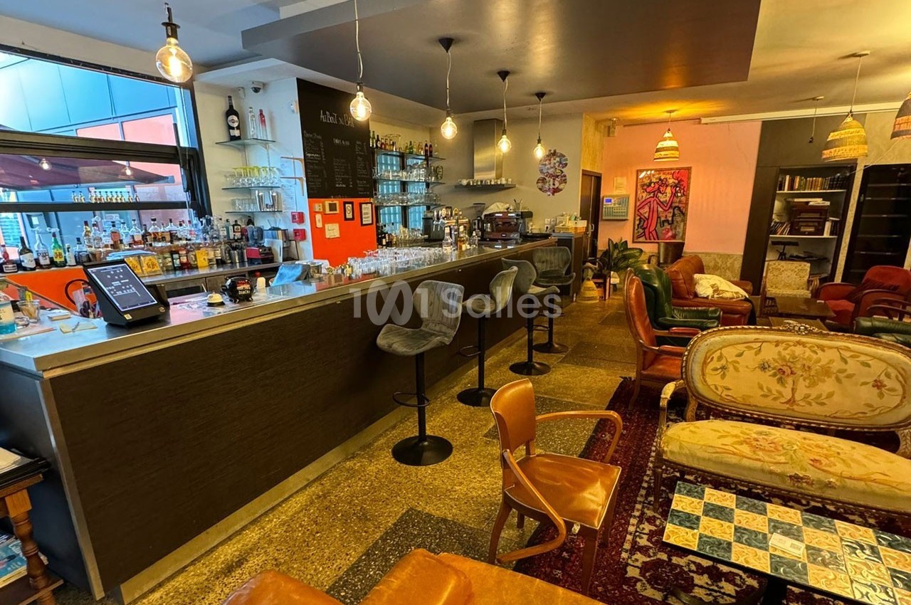 Intérieur d'un bar chaleureux avec un comptoir, des tabourets, des canapés et une décoration éclectique.