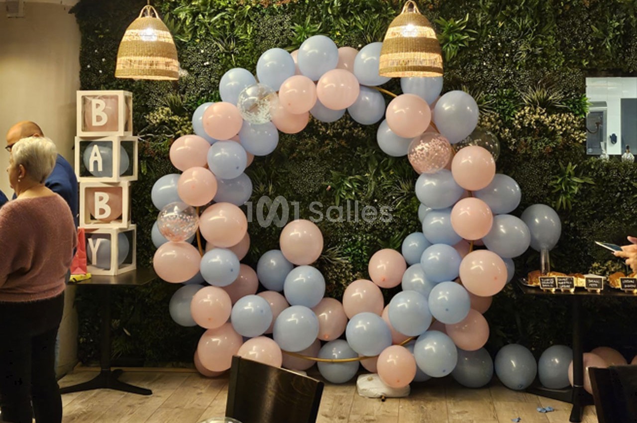Décoration avec arche de ballons roses et bleus devant un mur végétal, cubes ’BABY’ et ambiance festive en intérieur.