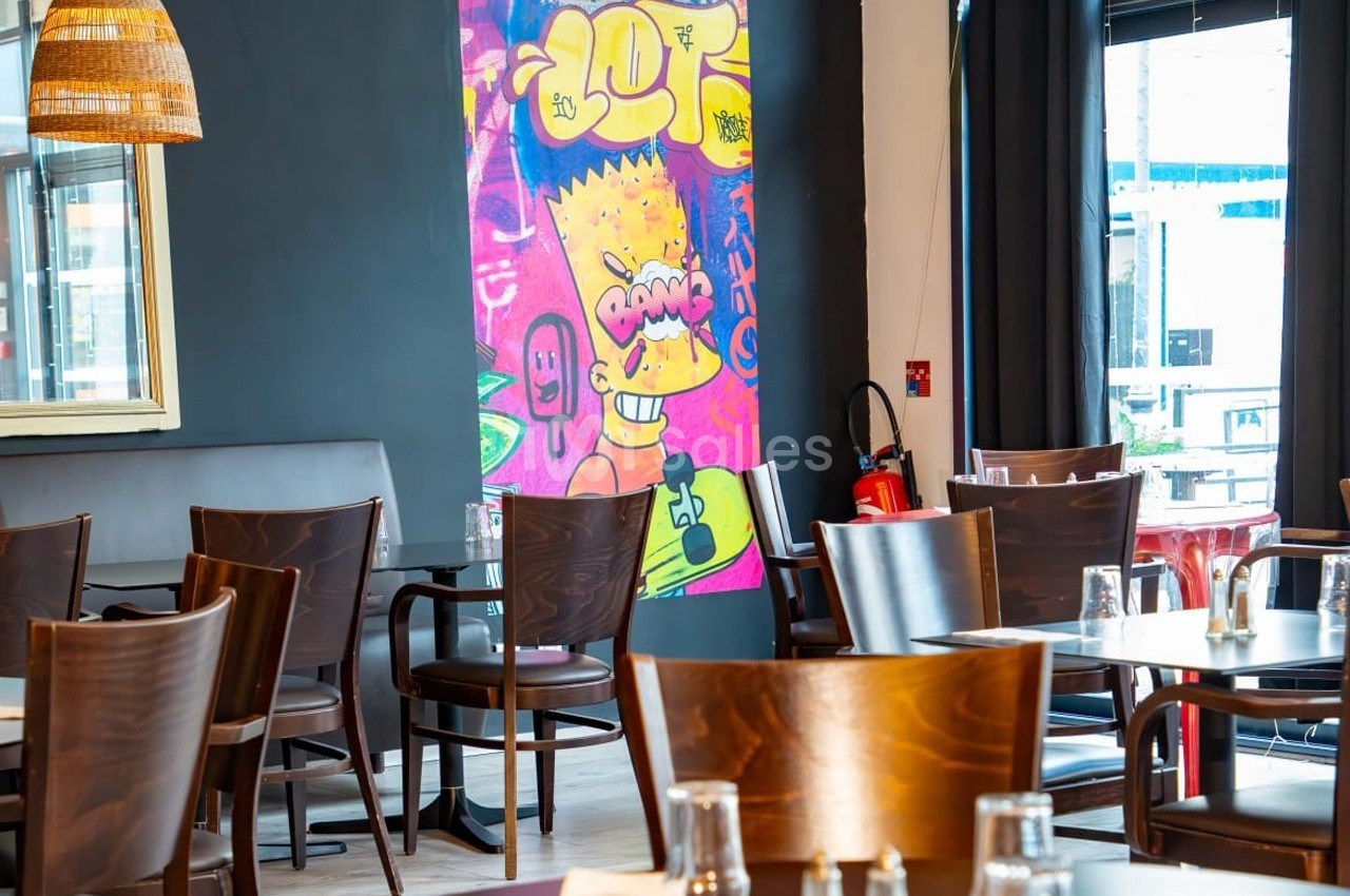 Salle de restaurant moderne avec des chaises en bois, tables dressées et un mur décoré d'une fresque colorée.