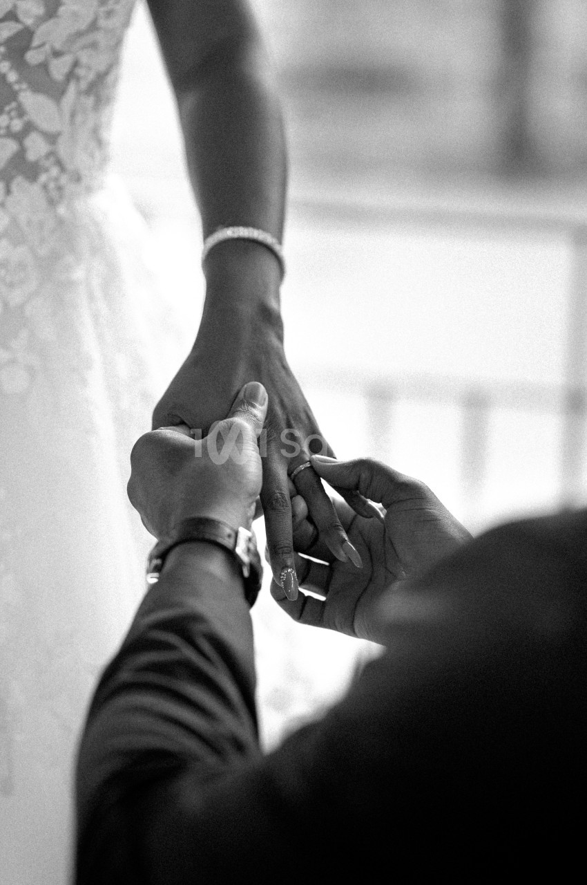 Un homme glisse une bague au doigt d'une femme en robe de mariée, capturé en noir et blanc.
